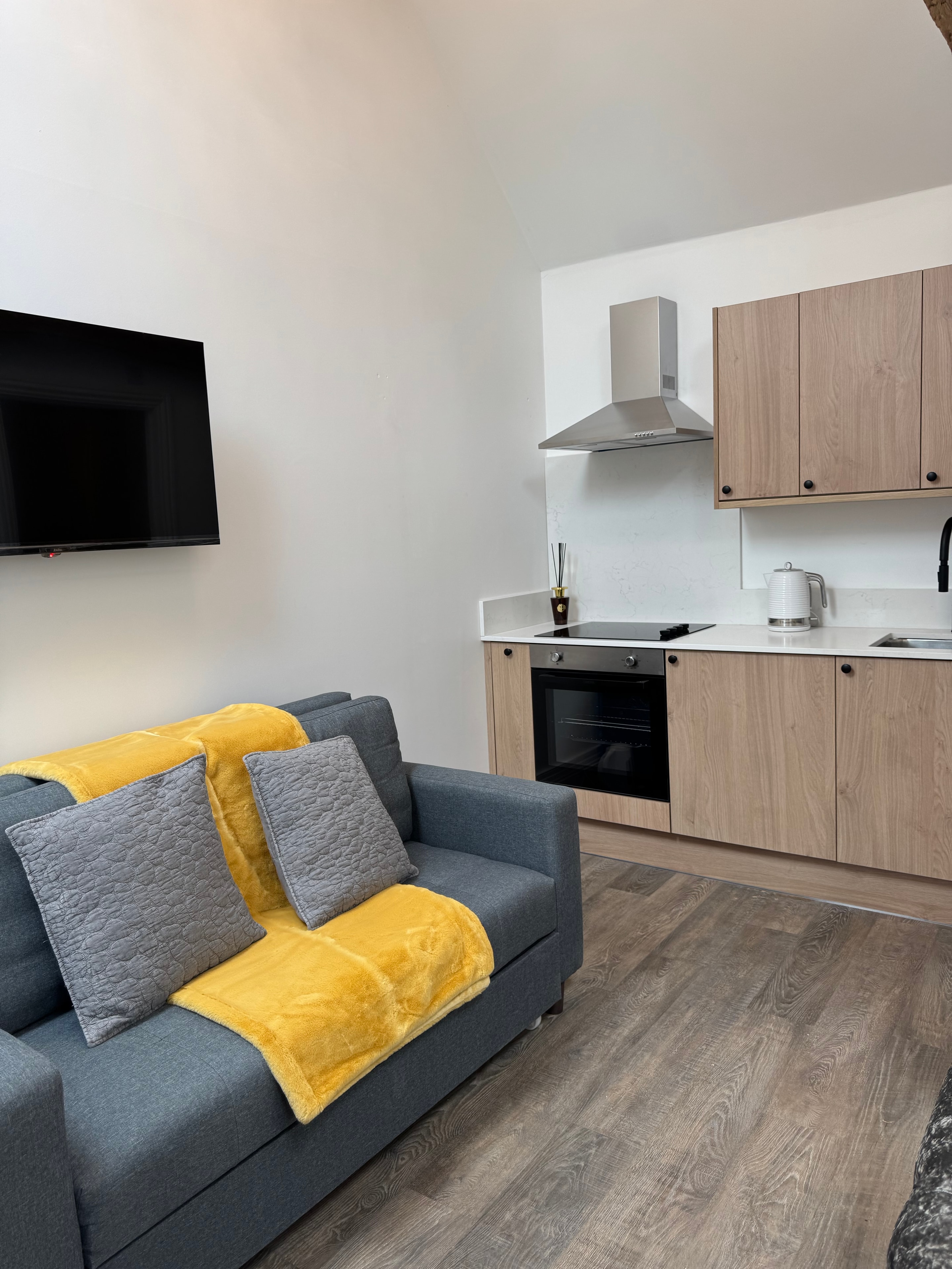 Living area with grey sofa, yellow accents and kitchenette